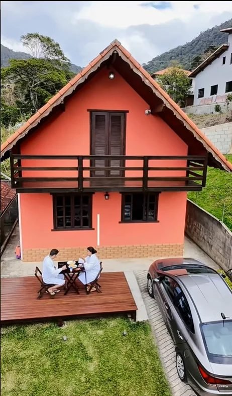 Chalé vermelho com o casal tomando café na varanda